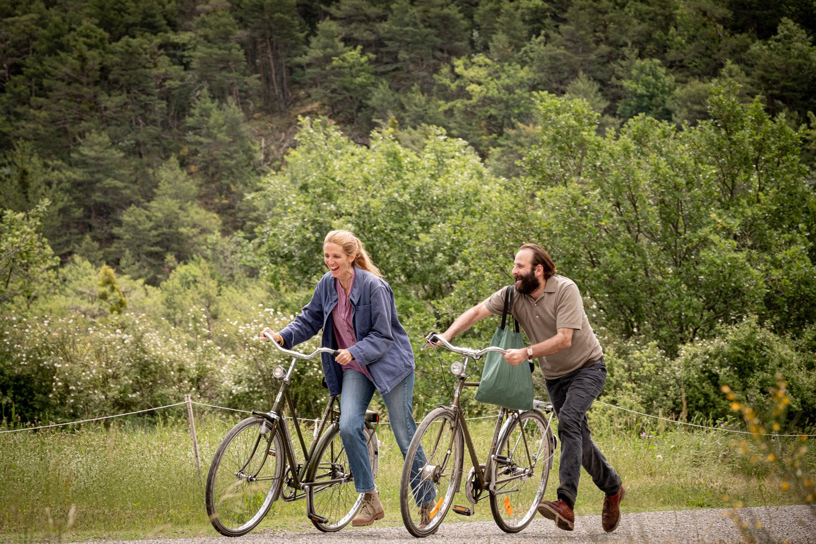 Sandrine Kiberlain et Vincent Macaigne poussent leur vélo sur un sentier de forêt en riant